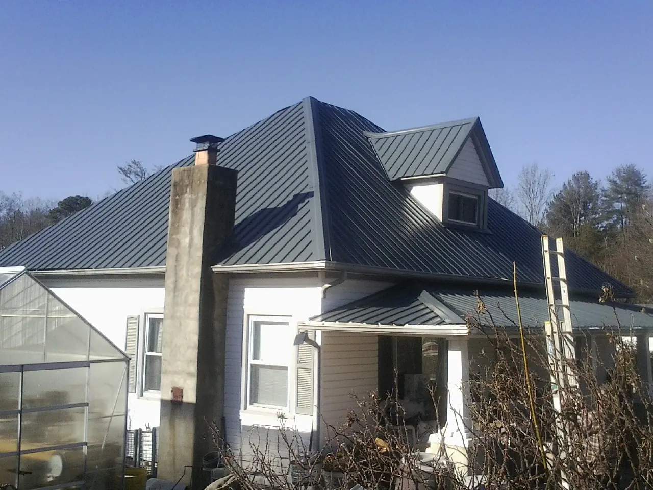 Dark blue standing seam metal roof on a white farmhouse with dormer — Slate & Tile Roof Repair by Roofing Brothers in Jetson