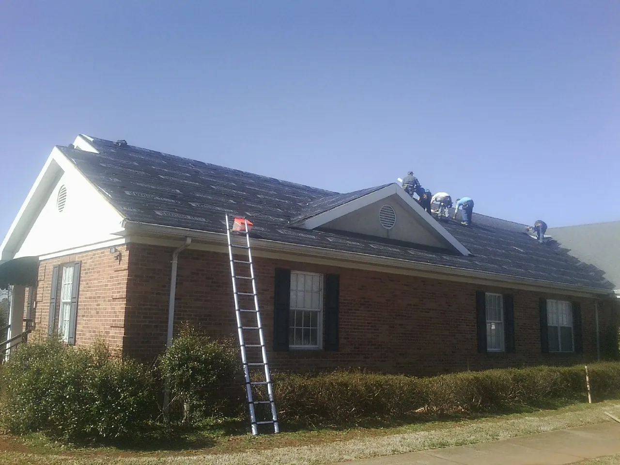 Crew tearing shingles off a brick ranch roof with a ladder set — Emergency Roof Repair work by our crew in Jetson