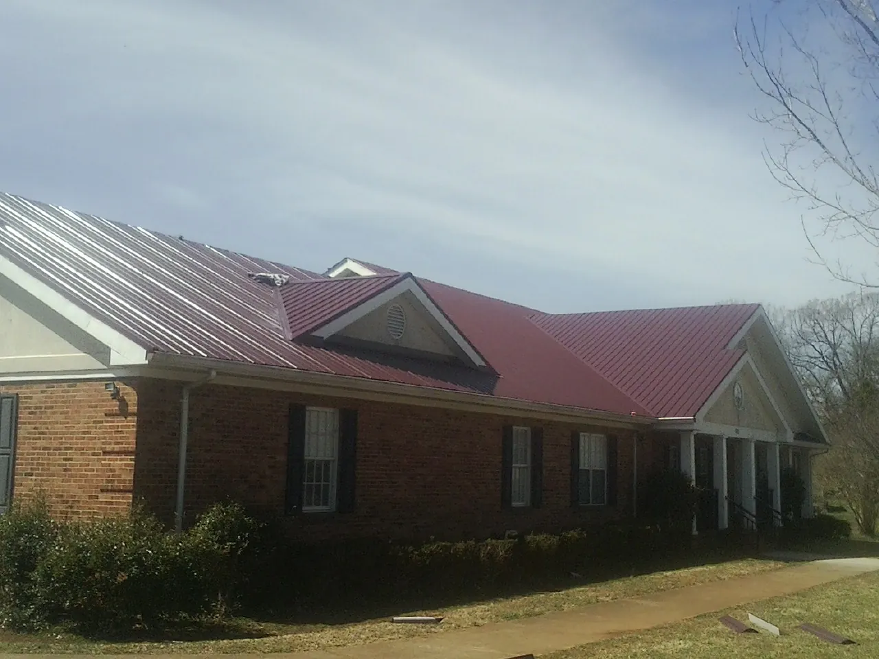 Red metal roof with gabled entries on a long brick building, from a Hail Damage Roof Repair job in Jetson