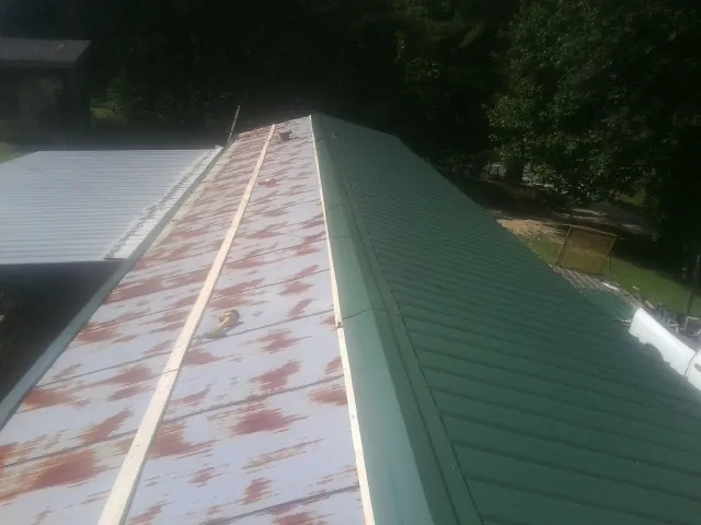 Old rusted panels beside newly installed green metal roofing — Wind Damage Roof Repair by Roofing Brothers in Jetson