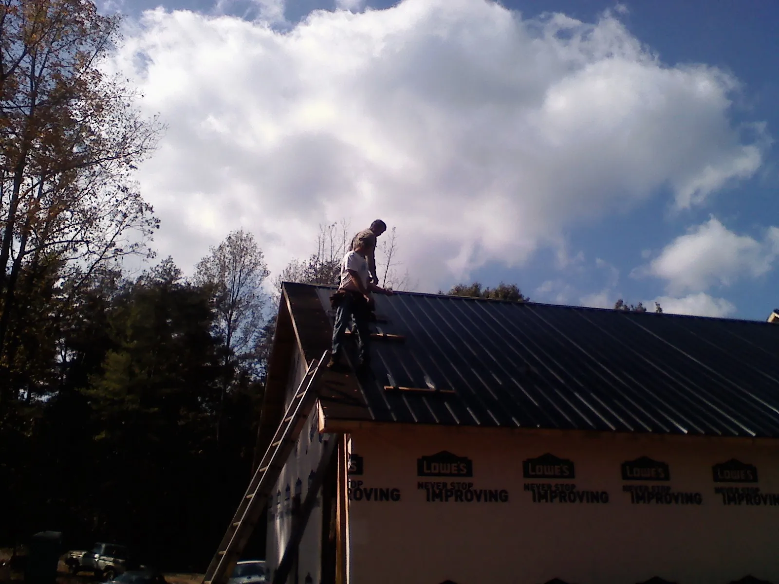 Roofer fastening dark metal panels high against a cloudy sky, from a Roof Inspection job in Jetson