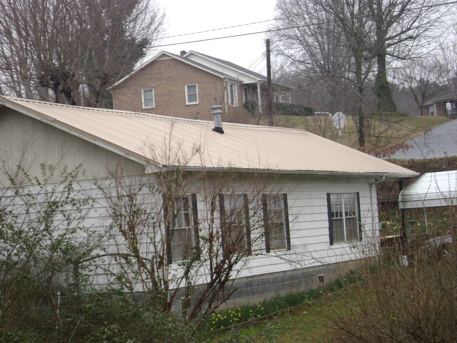 Tan metal roof on a white sided house set into a hillside — Commercial Roofing by Roofing Brothers in Jetson